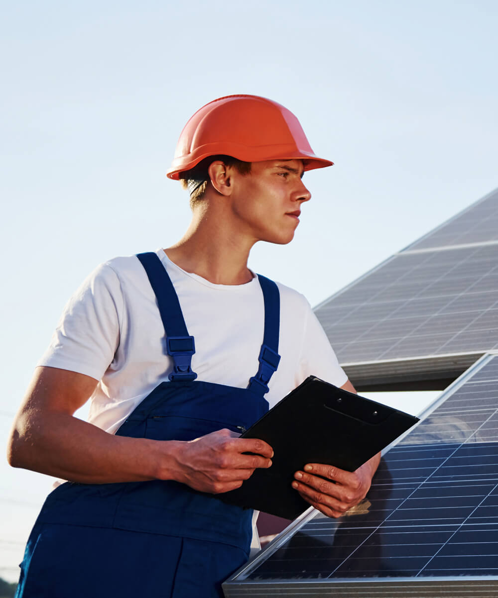 A man in an orange helmet is holding a clipboard.