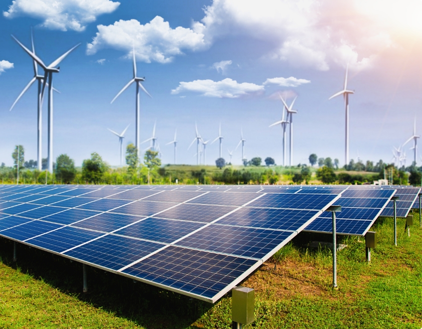 A field with many solar panels and wind mills.